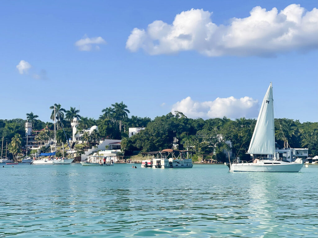 Boats on the water of Bacalar Lagoon with greenery and structures on land in the distance.