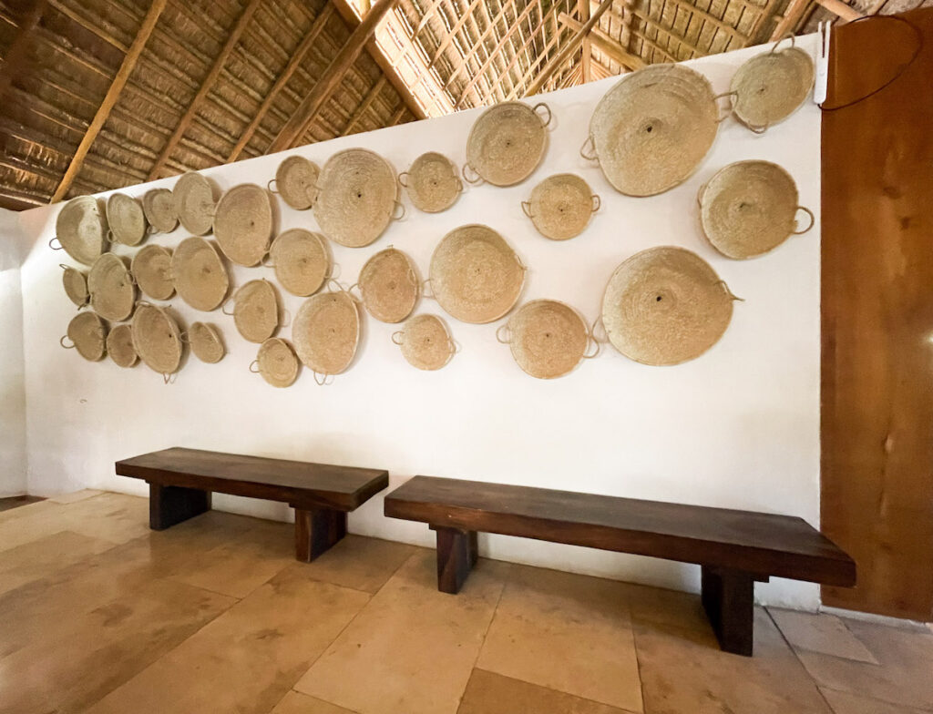 A wall decorated with several flat baskets and two low benches beneath.