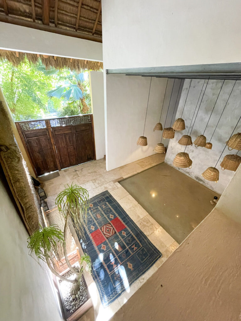 A downward view on the foyer with a pond, hanging basket light fixtures, a potted palm tree, and a patterned carpet at Casa Hormiga Bacalar.