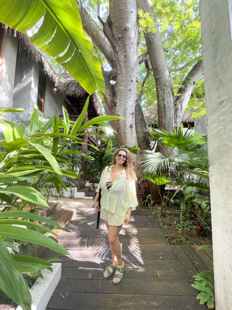 A woman posing on a wooden deck surrounded by a jungle landscape on the the grounds of Casa Hormiga Bacalar.