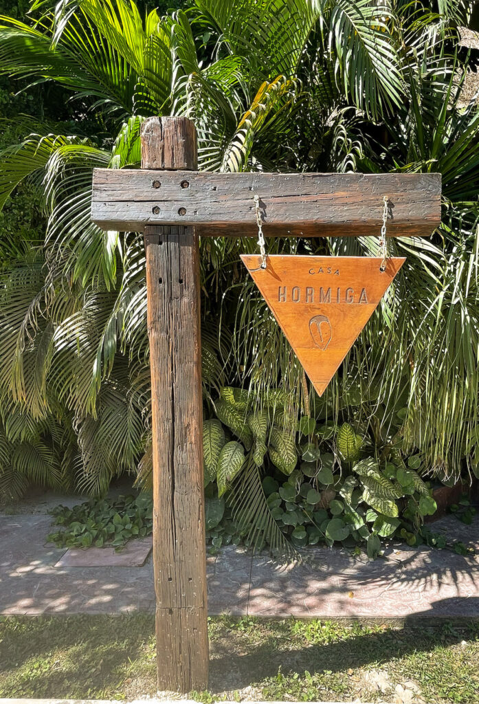 A triangular sign hanging from a wooden frame announcing Casa Hormiga Bacalar