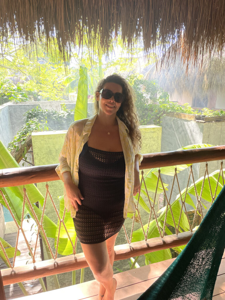A woman standing outside on the terrace with a background of plants and cement walls at Casa Hormiga Bacalar.