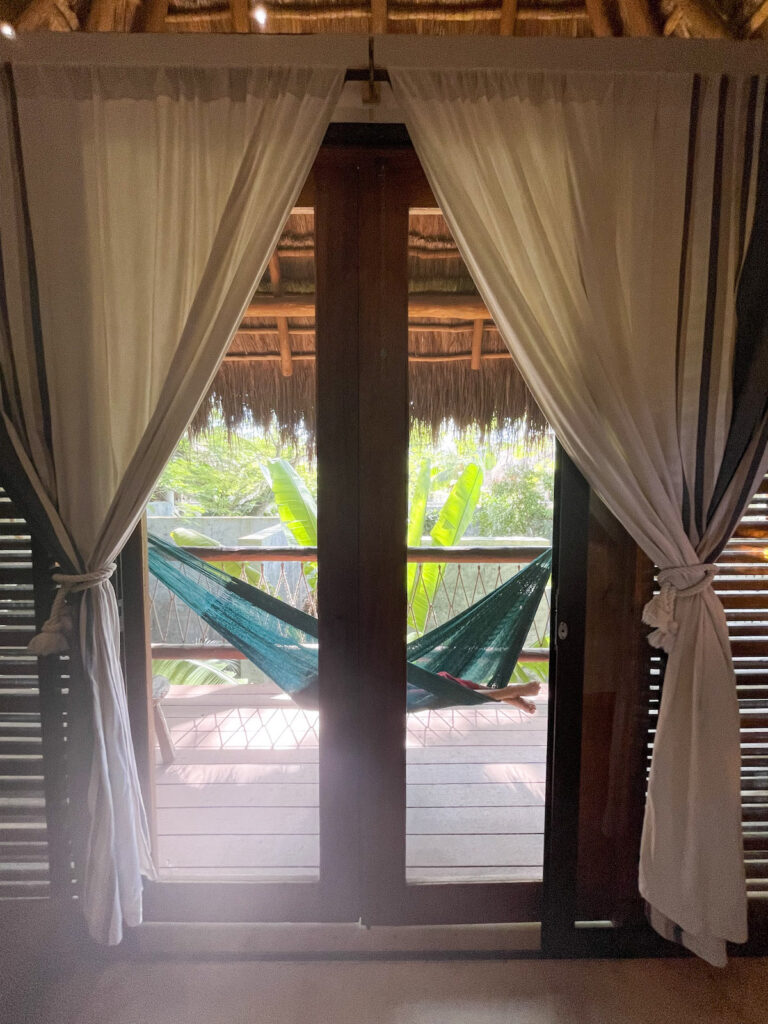 A hammock as seen through a pair of closed glass doors and framed by curtains.