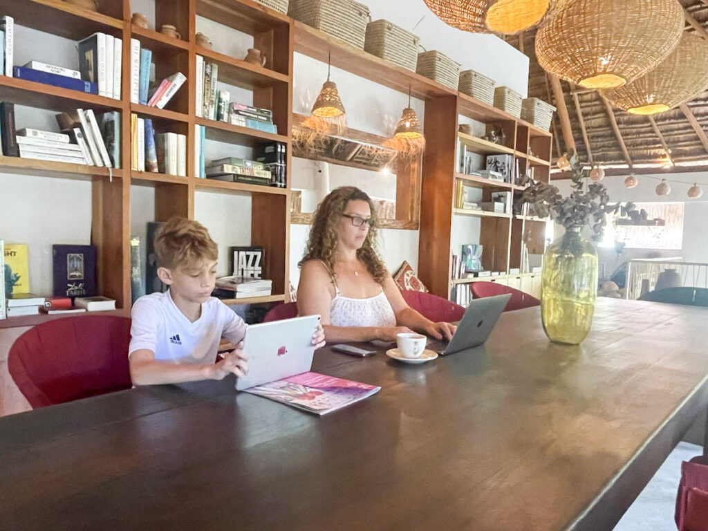 A woman and a boy sitting at a table working on an Ipad and computer.
