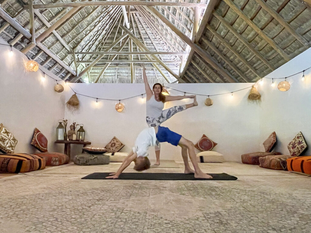 A woman doing standing leg yoga pose and a boy in front of her doing a backbend on all fours.